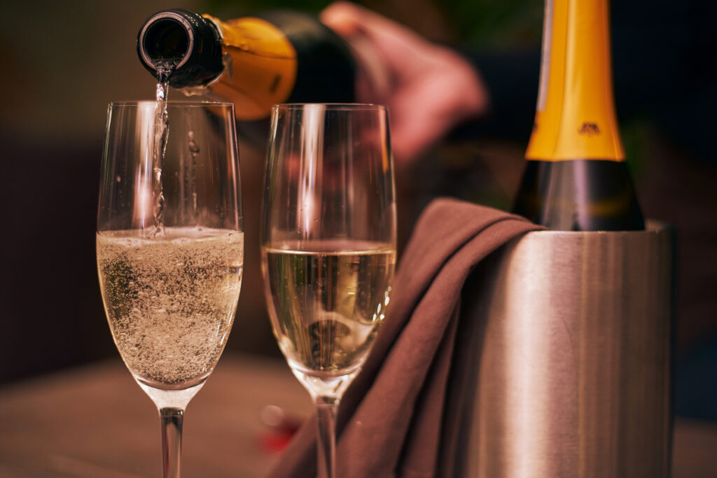 Close up shot of pouring champagne into two glasses, detail, bubbles