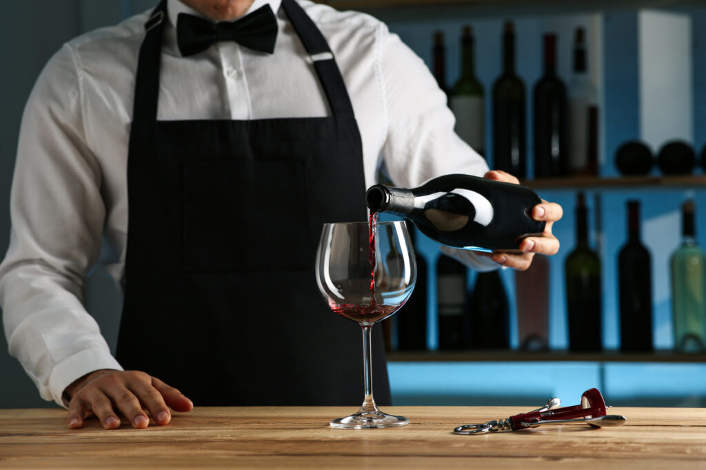Bartender pouring wine into glass at counter in restaurant, closeup