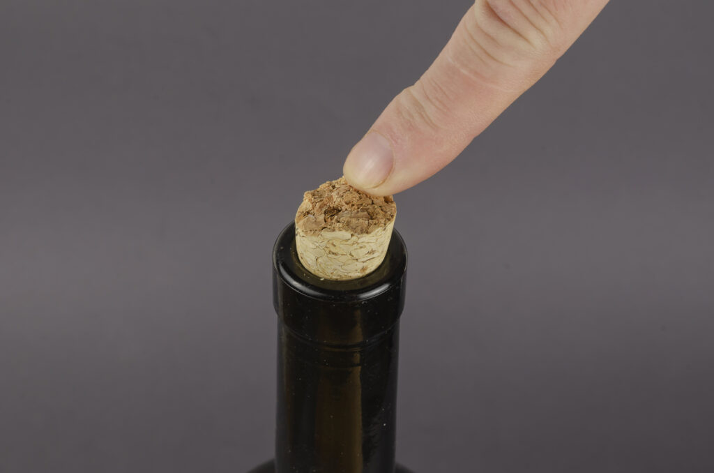 Wine bottle with broken cork and finger on gray background. The index finger of a man's hand points to a broken cork.