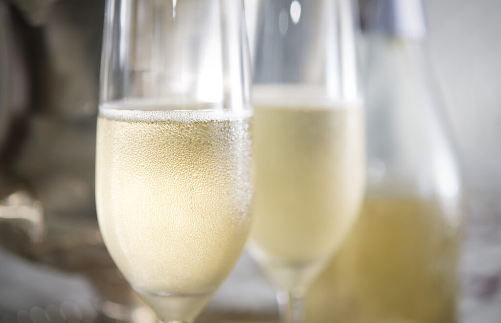 Closeup of two flutes of champagne with bubbles and droplets of condensation with silver ice bucket and bottle in background.
