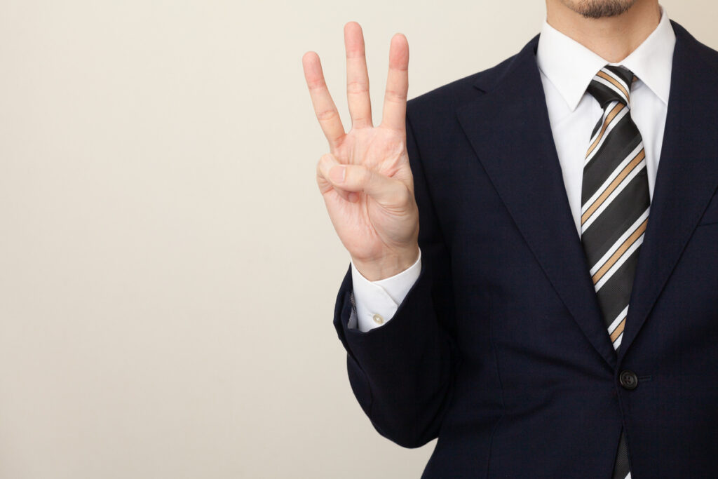 A man in a suit with three fingers, white background
