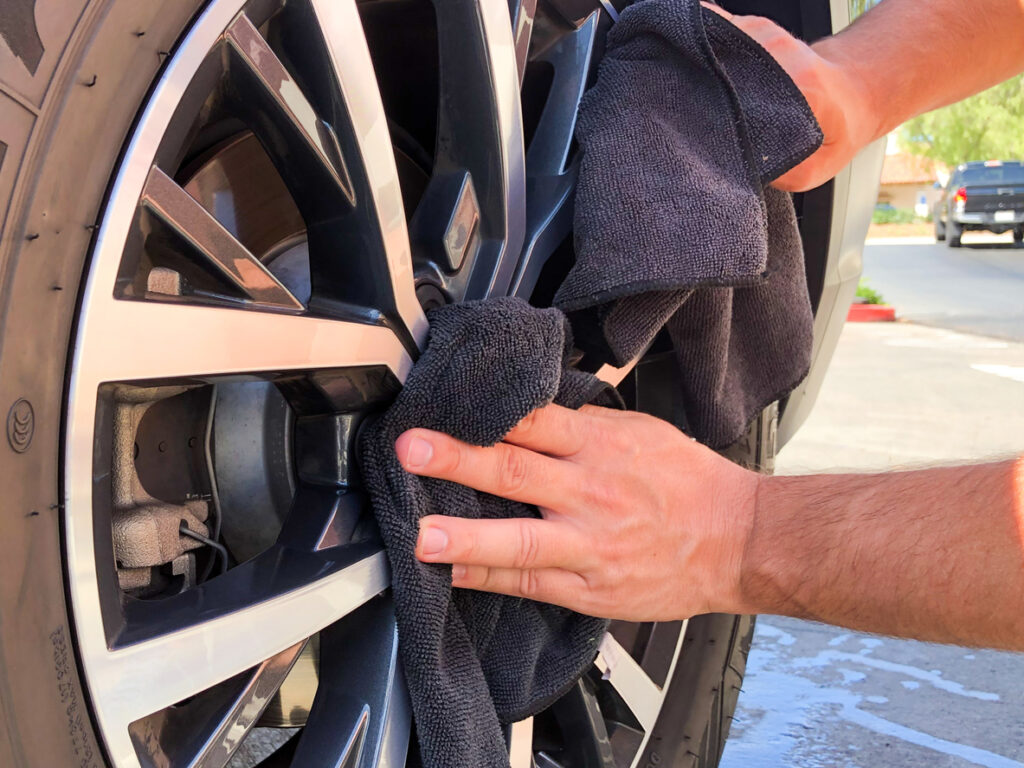 Man's hand cleaning wheel and tire with black microfiber cloth. Hand wipe down shiny rims surface of car. Car detailing and car wash concept