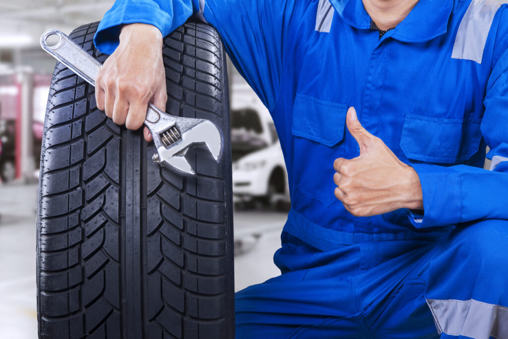 Technician with a blue workwear, holding a wrench and a tire while showing thumb up