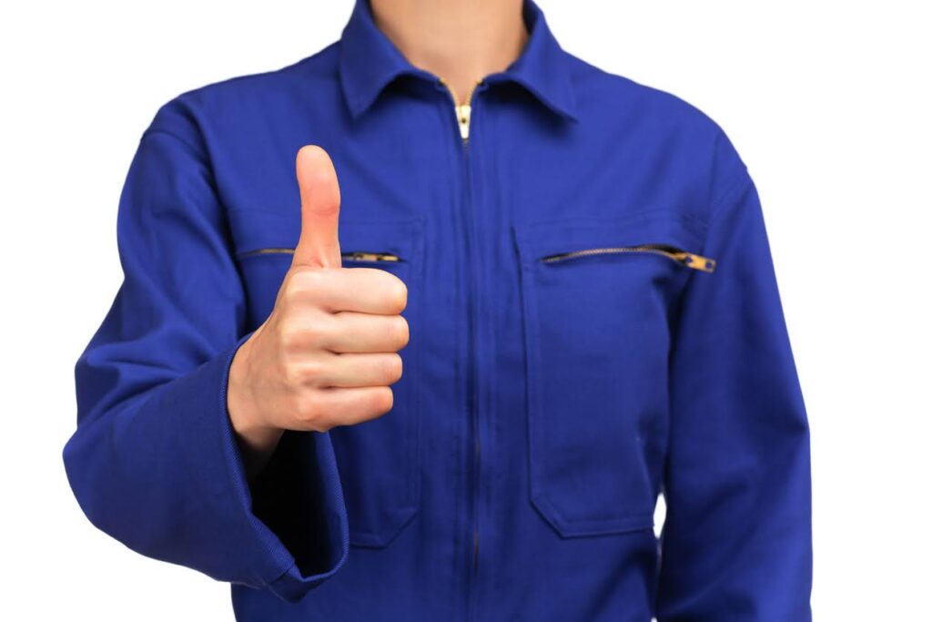 photograph of a bust of a woman in blue work uniform making the OK sign