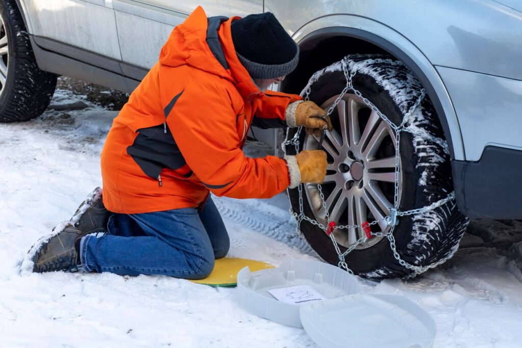 A medium shot of a senior, Caucasian man fixing snow chains onto his car tyres.