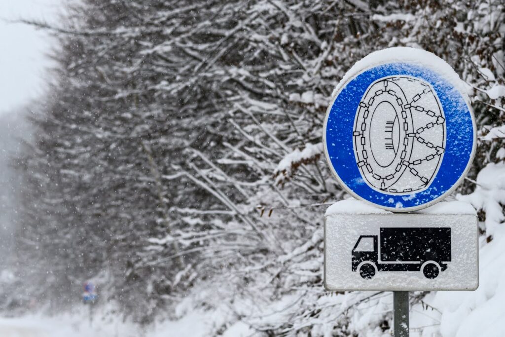 Road sign with depicting tire chain and a truck on a snowbound road in wintertime.